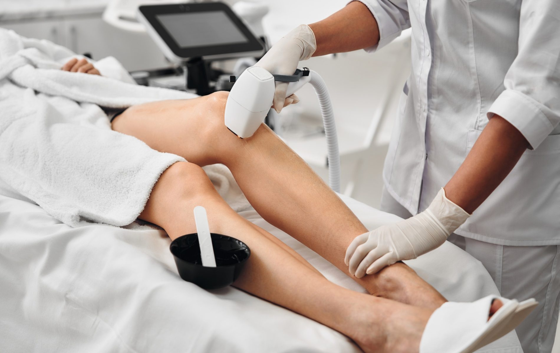 Aesthetician performing laser hair removal on a clients leg in a clinic